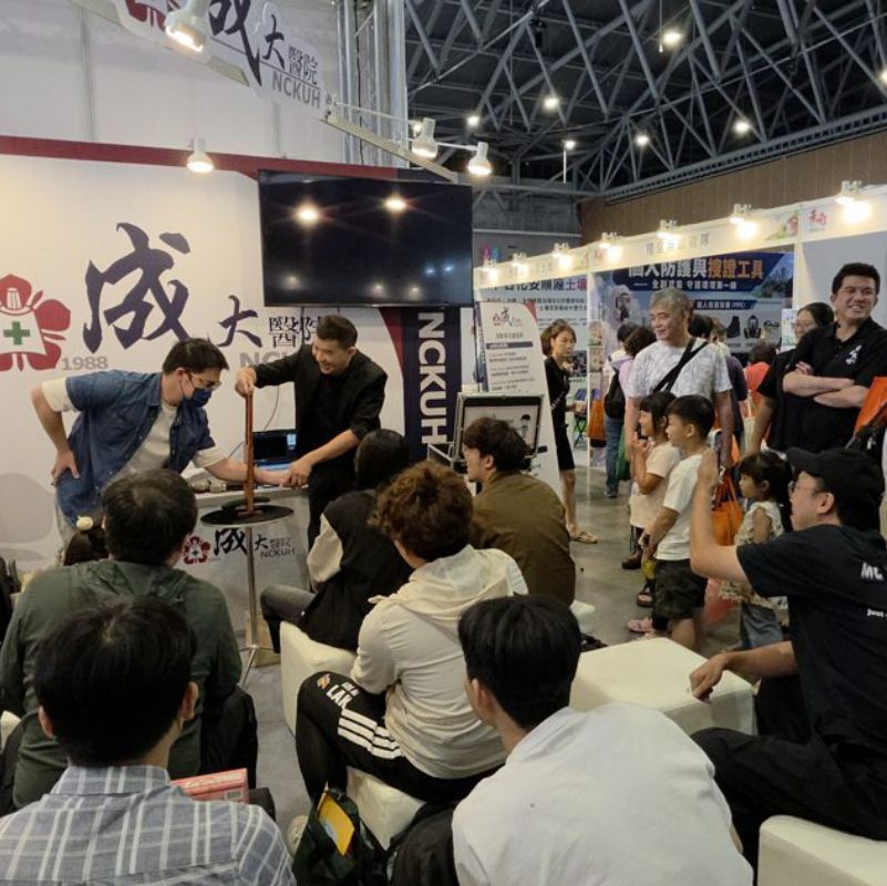 李貫廷醫師在成大醫院攤位前與一位民眾互動表演，周圍大小朋友圍觀